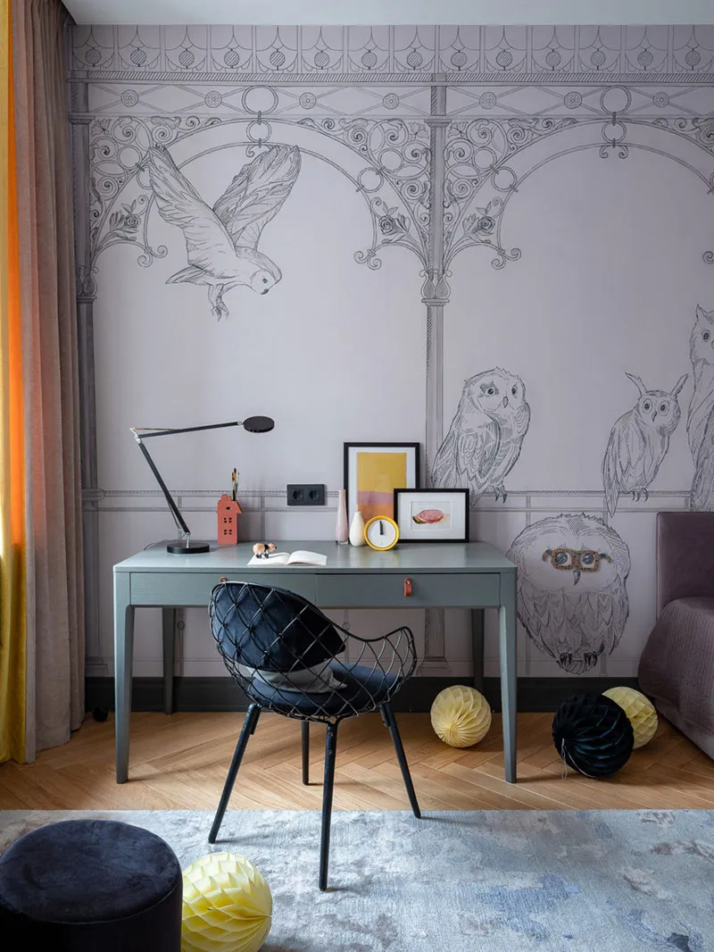 A modern home office with a grey desk, black chair, and a wall decorated with intricate grey owl sketches.