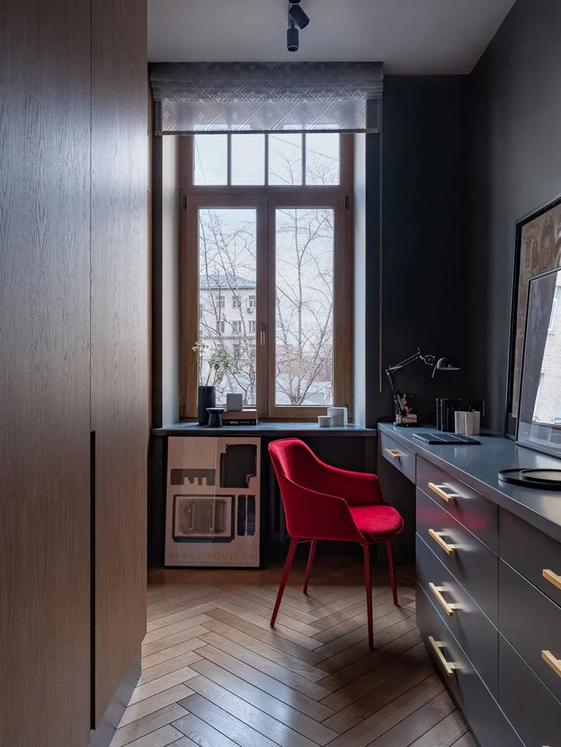 Modern home office with a red chair, window seat, and dark wood flooring.