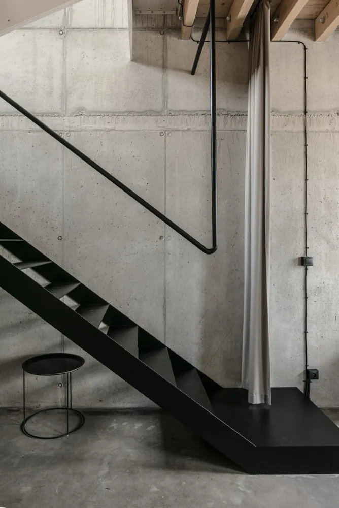 Modern industrial staircase with black metal railing and concrete steps against a raw concrete wall.