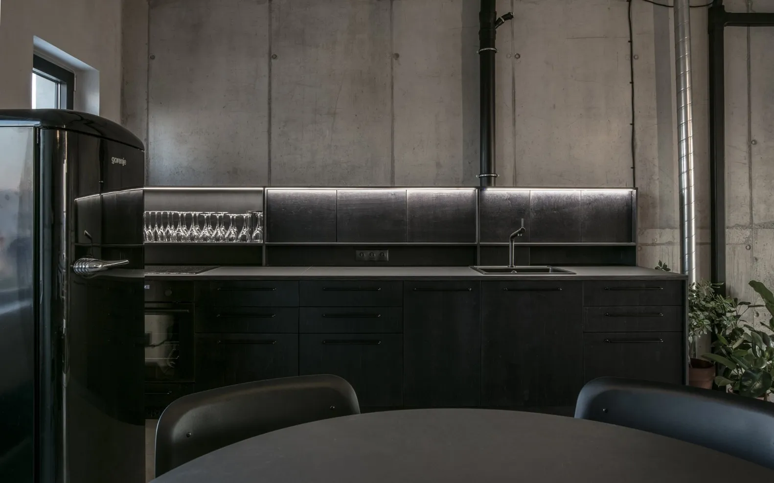 A modern kitchen with metal cabinets, black countertops, and a black refrigerator.