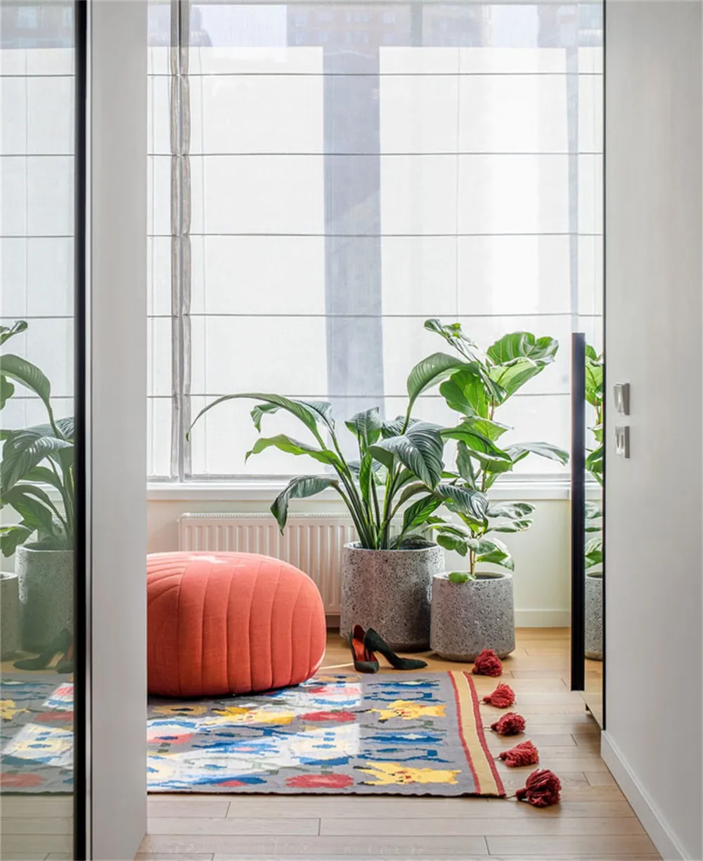 An industrial living area featuring a concrete planter, green potted plants, and an orange cushioned stool over a colorful pa