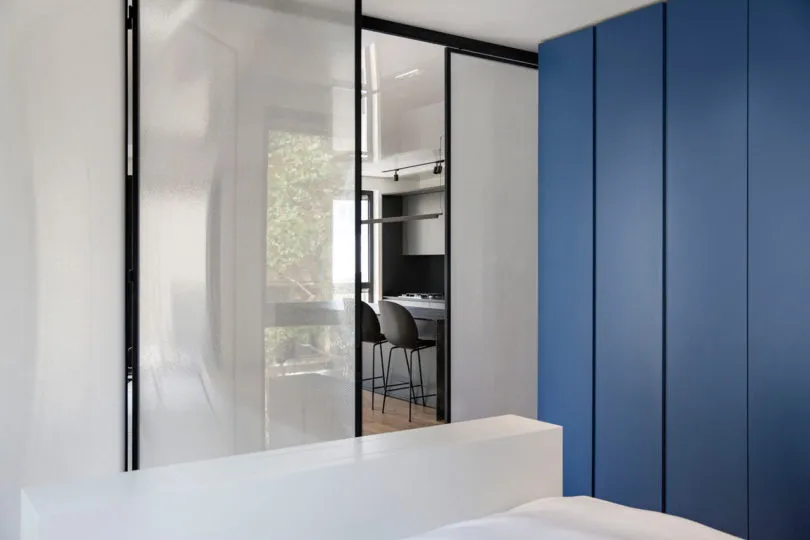 Modern, minimalist bedroom with glass walls and blue storage cabinets.