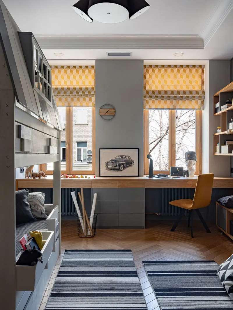 Minimalist home office with a wooden desk, yellow geometric window shades, and a grey and white striped rug.