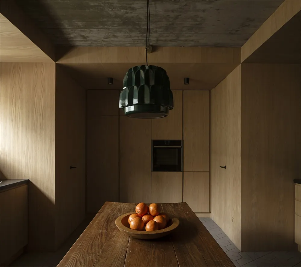 A minimalist residential kitchen featuring wooden cabinets and a wooden dining table with a bowl of oranges.