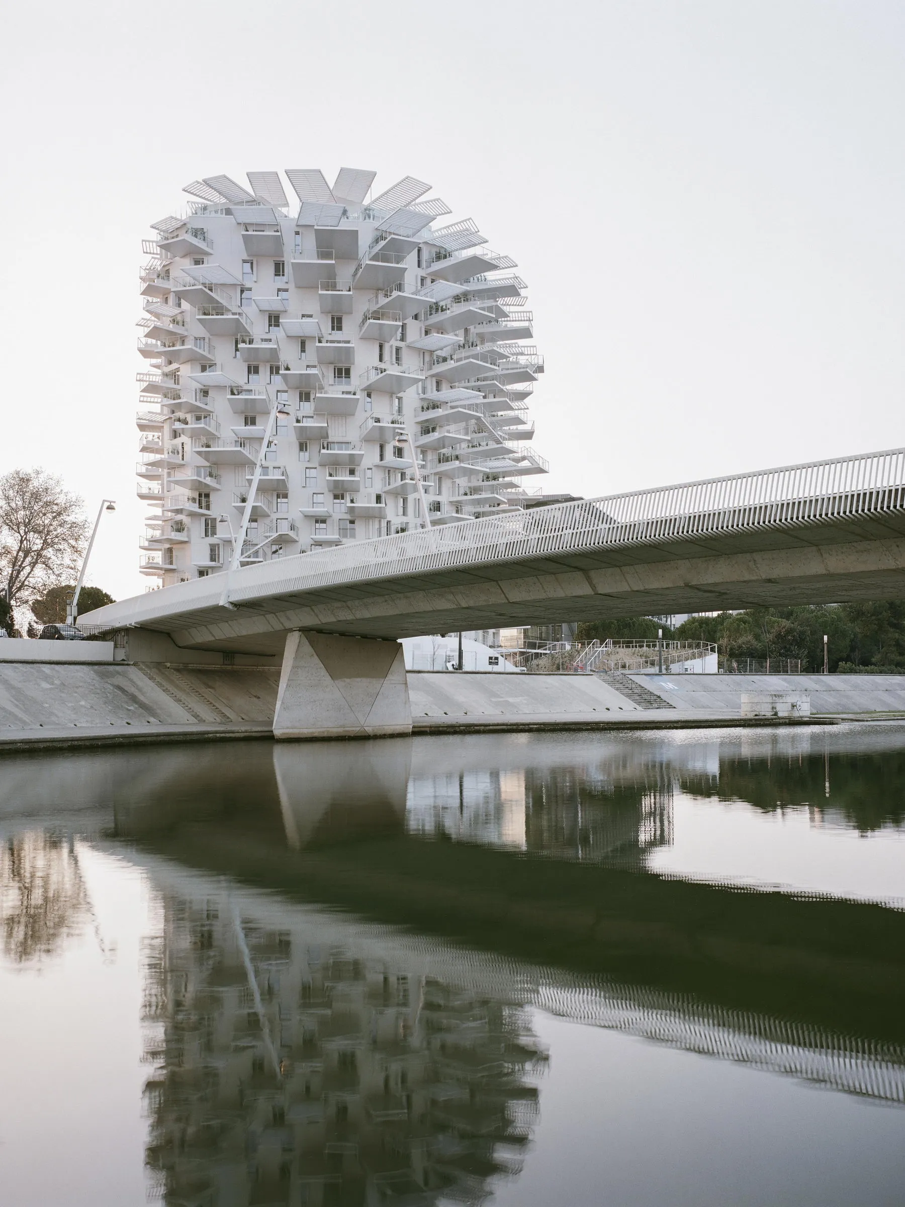Concrete building with geometric balconies reflected in calm river waters, modern architectural style.