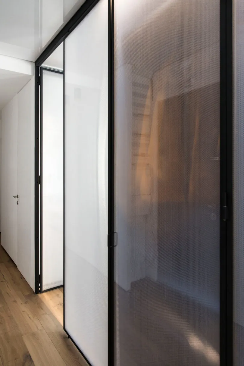Modern interior space featuring glass partitions on white walls and wooden flooring.