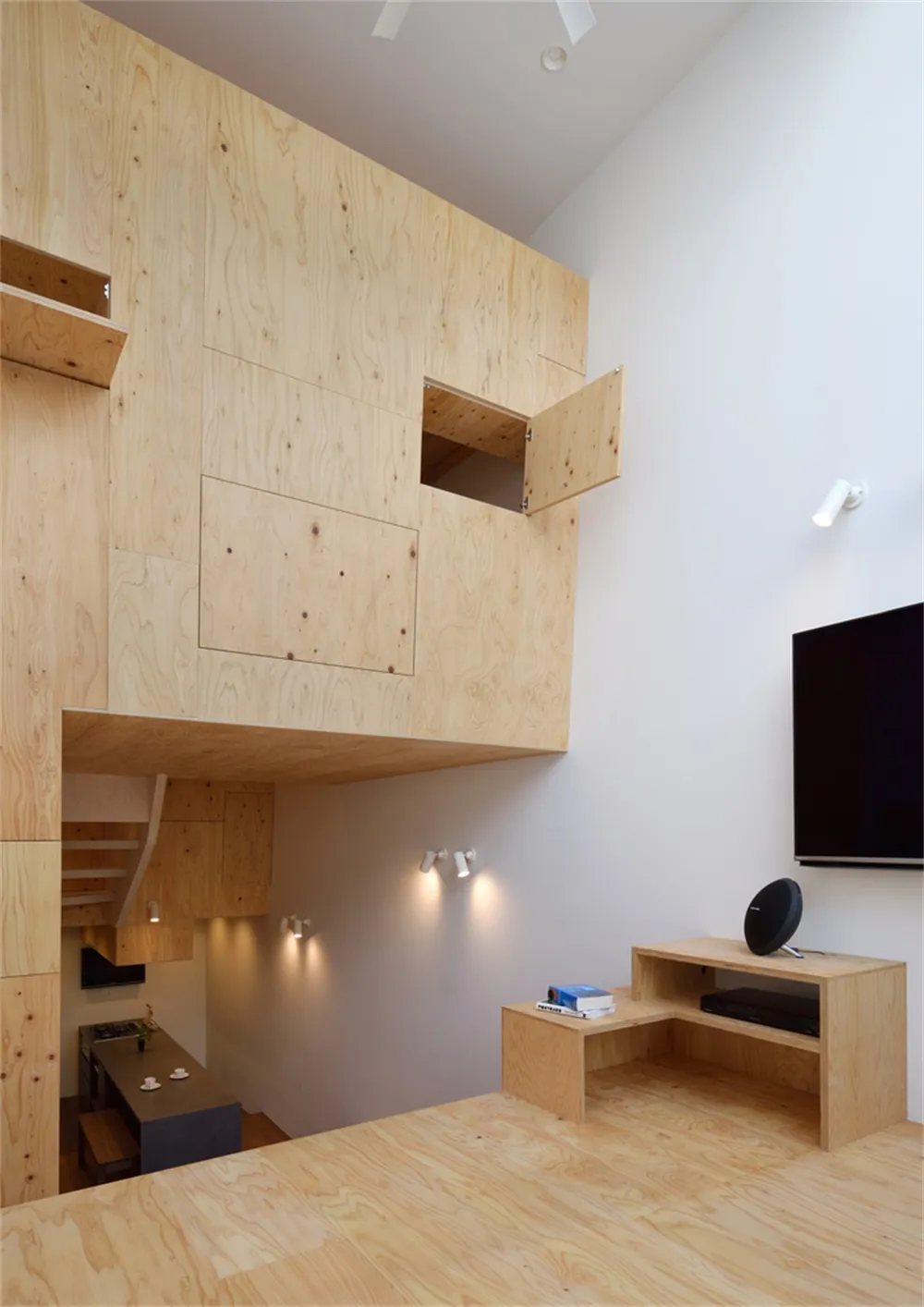 A modern living room featuring wooden paneling with a loft space and integrated furniture and lighting.