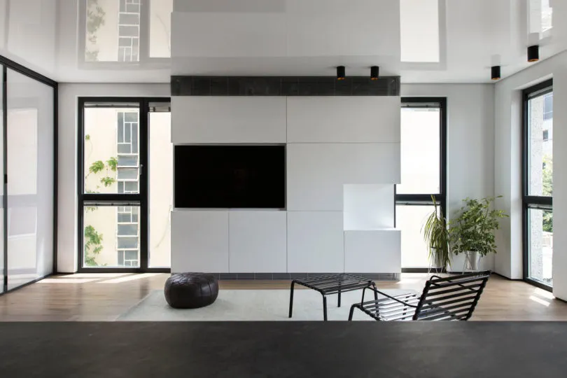 Modern minimalist living room with white walls, black furniture, and large windows
