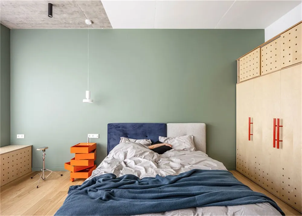 A modern bedroom featuring a bed with a blue headboard, grey bedding, and orange accent furniture.