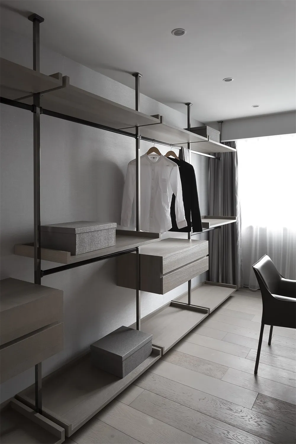 Modern closet with wooden shelves and metal rods, featuring a minimalist design with gray and white colors and a window.