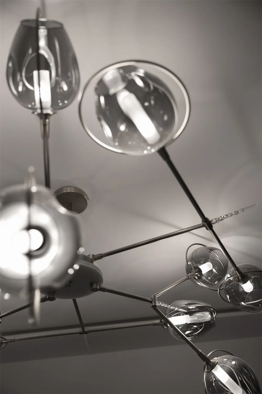 Modern lighting fixture with glass shades hanging from metal rods against a gray background.