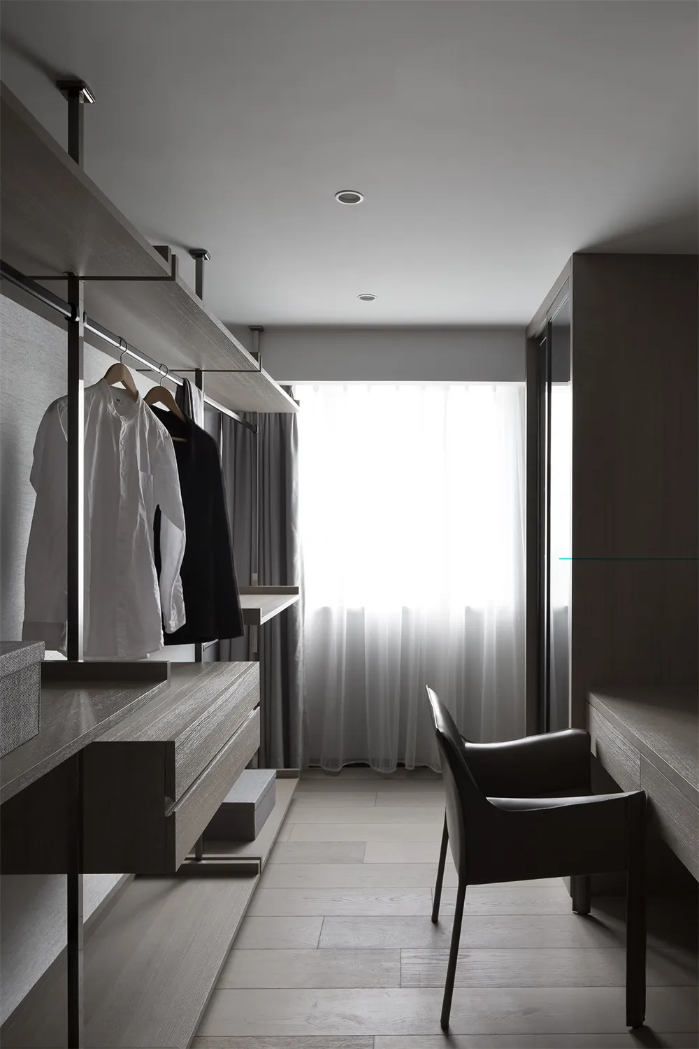 A minimalist closet with wooden shelves, white curtains, and a white chair by the window.