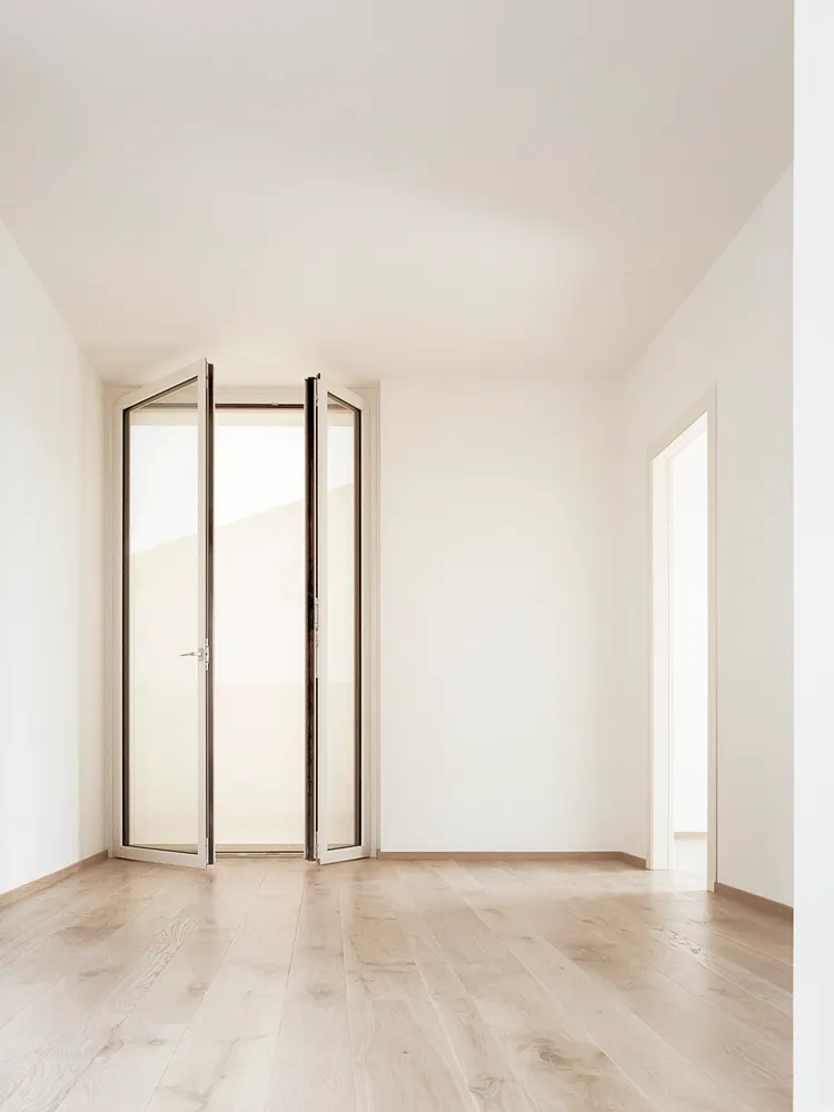 An empty room with minimalist design, featuring wood paneling and an open door leading to another room.