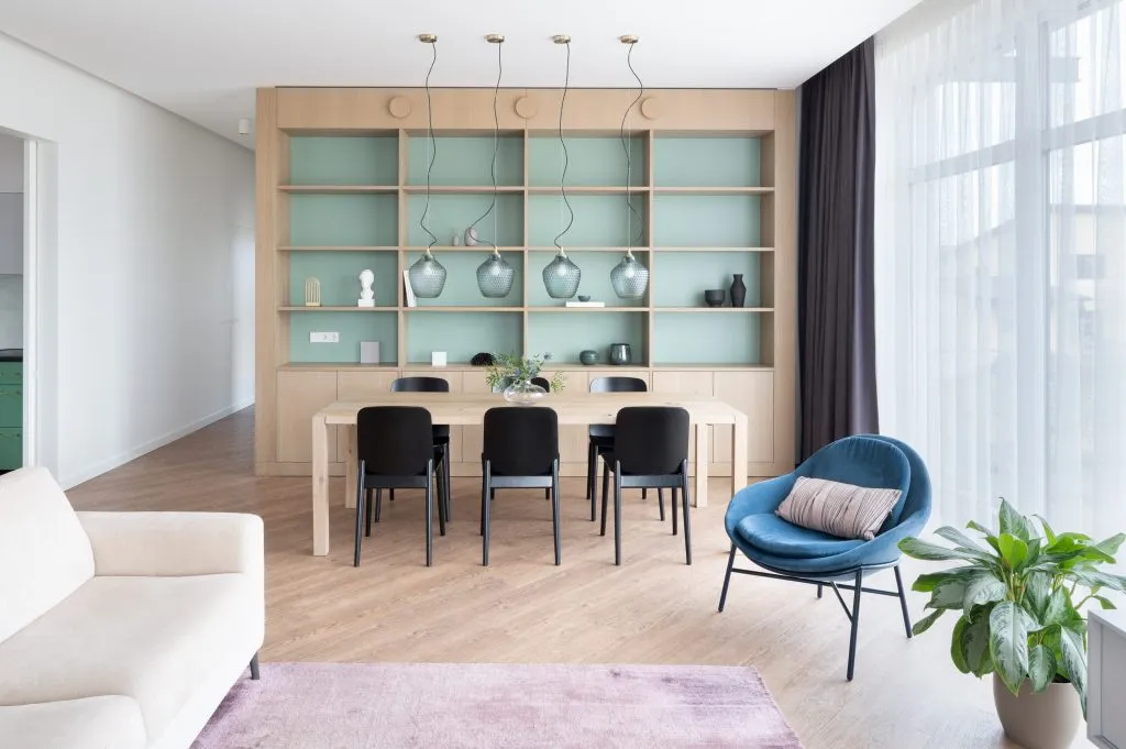 A minimalistic residential interior featuring wooden furniture, glass pendant lights, and soft textiles.