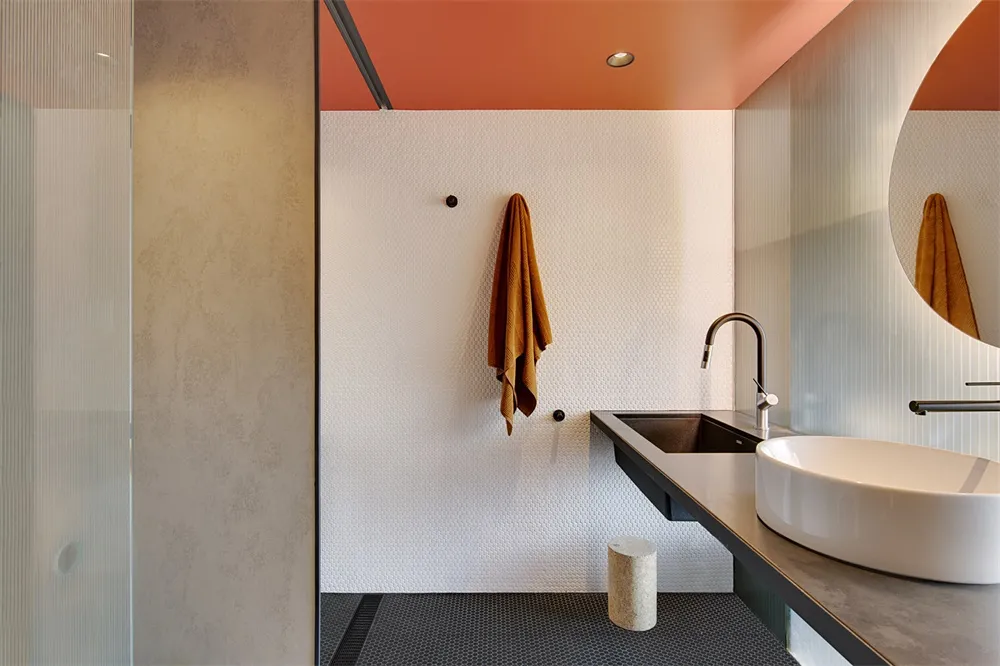 A modern bathroom with a concrete floor, white walls, and an orange ceiling.