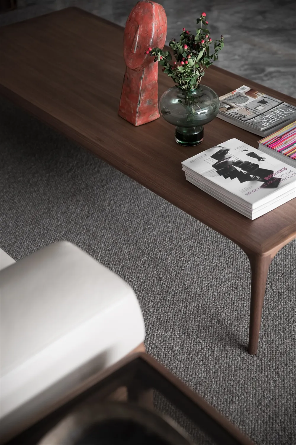 A sleek, modern coffee table crafted from wood, adorned with a red sculpture, green vase with red berries, and architectural