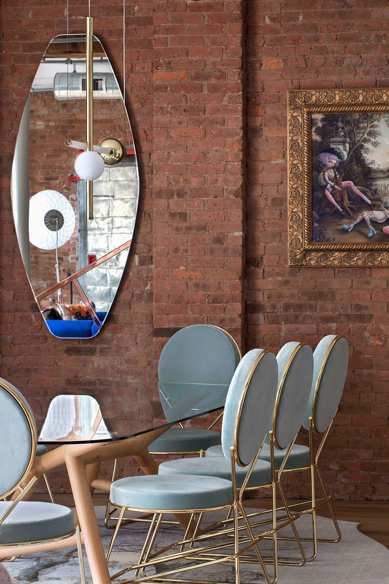 Modern dining room featuring glass table, metal chairs, and artwork on a brick wall.