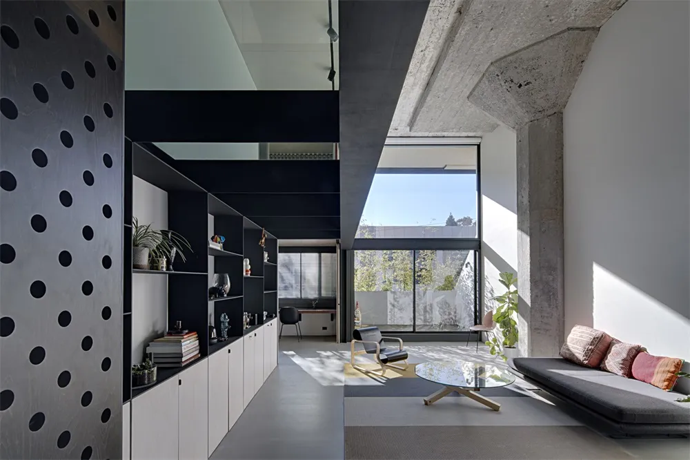 A spacious, modern living room with concrete walls and floor, featuring a sofa, coffee table, and bookshelf.