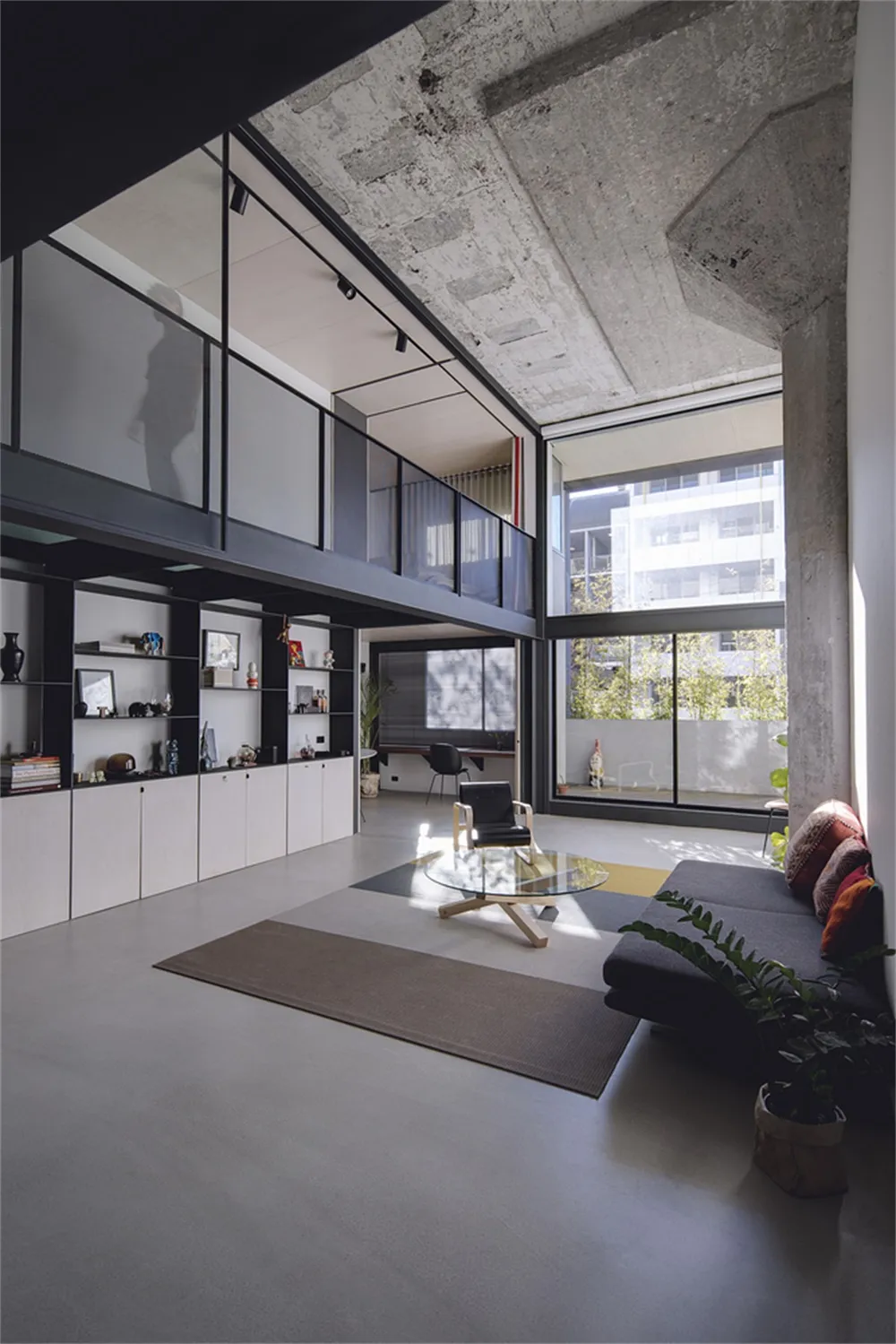 Modern living room with concrete flooring, glass coffee table, and minimalist decor.