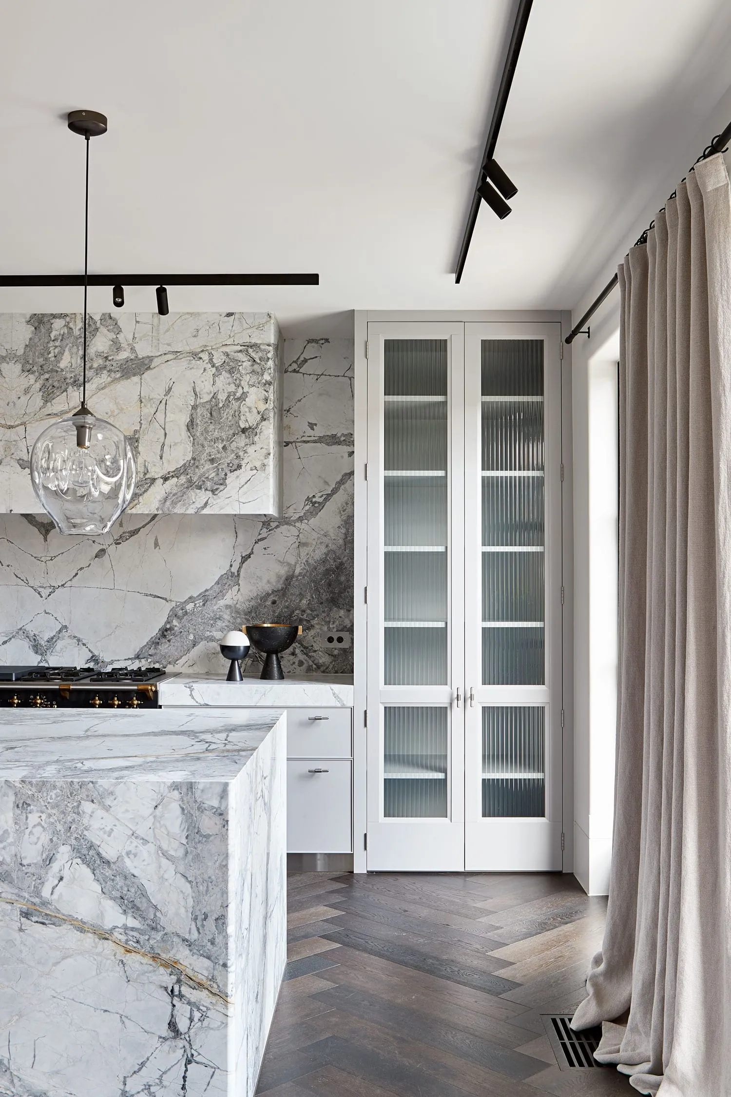 A modern kitchen with marble countertops and flooring, featuring white cabinetry and a minimalist design.