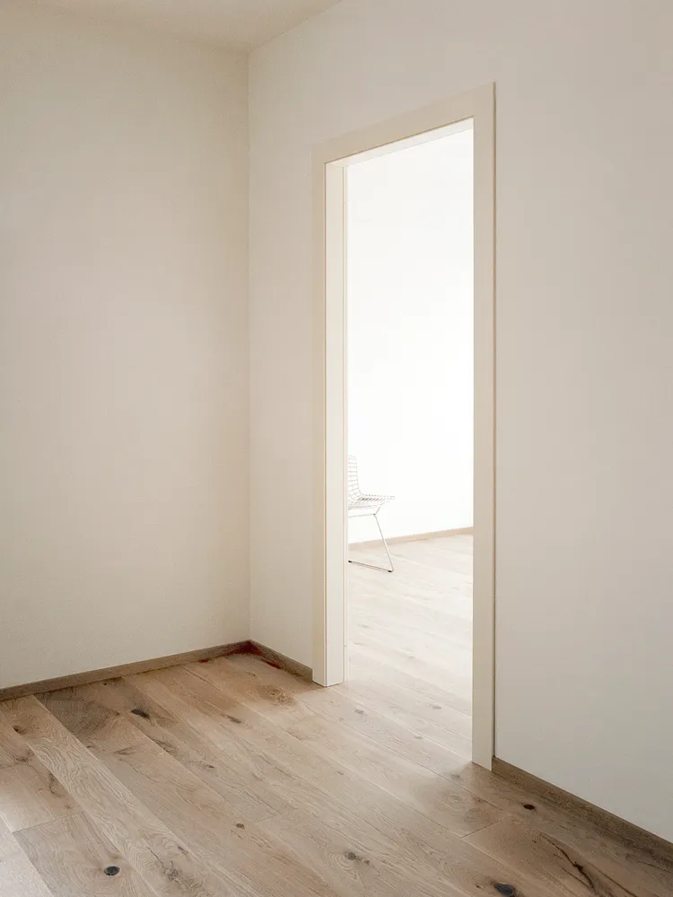 Minimalist interior with a white room, open doorway, and light wood flooring.
