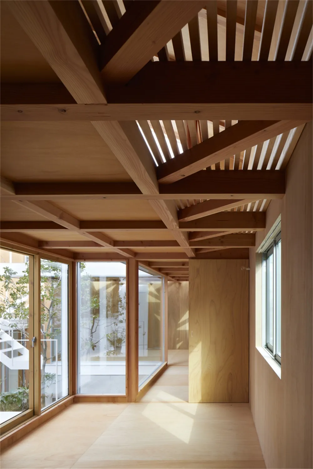 Modern residential interior with wooden floors and beams, featuring a well-lit space with large windows.
