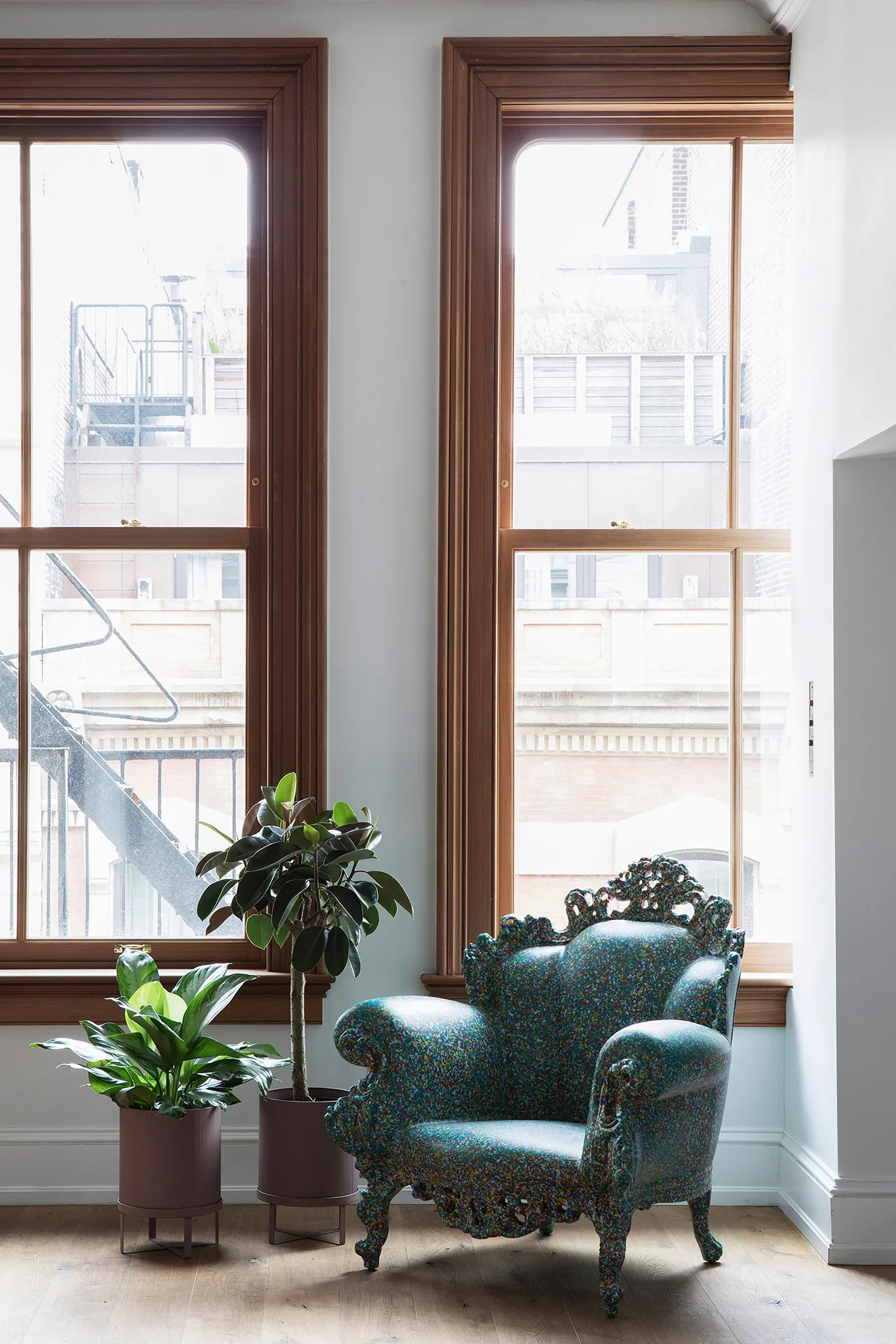 A modern, blue, scale-shaped armchair in a living space with a large window and plants.