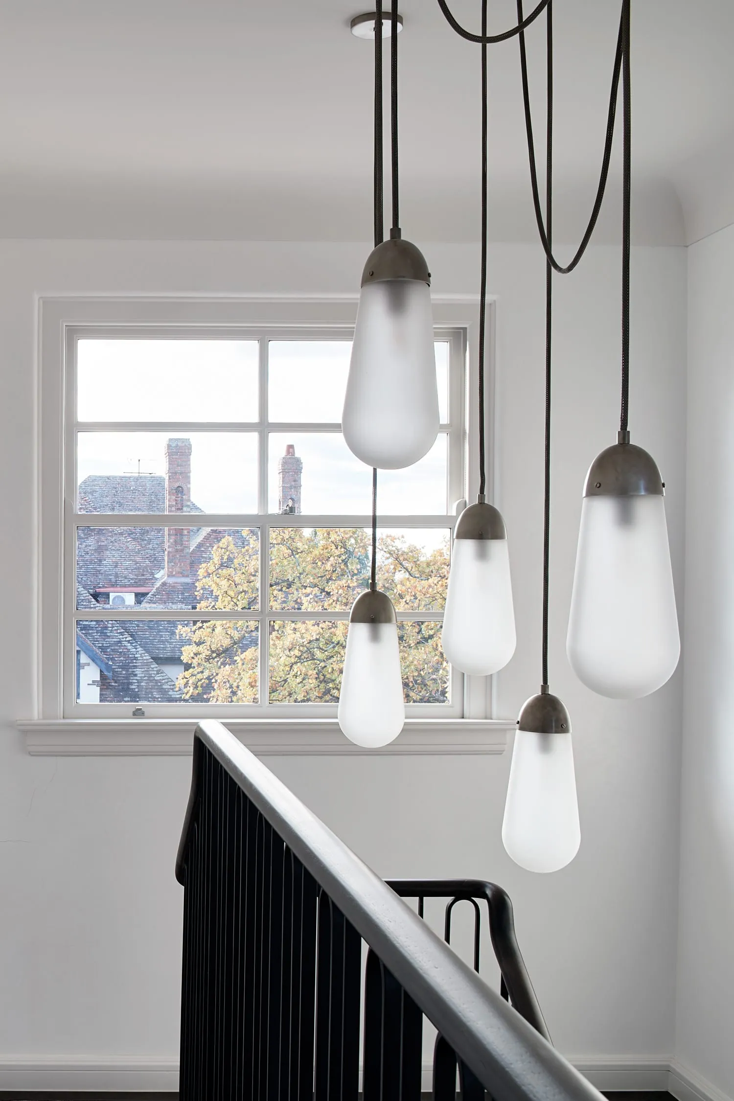 Modern staircase with glass railings illuminated by four frosted glass pendant lights with metal accents.