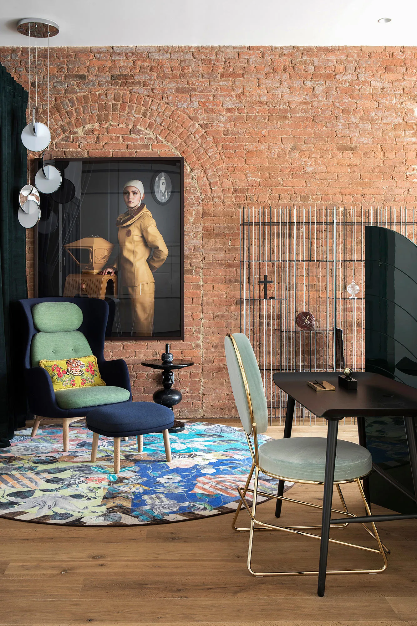 A modern industrial living room featuring brick walls, a round floral rug, and a combination of green and blue upholstered ch