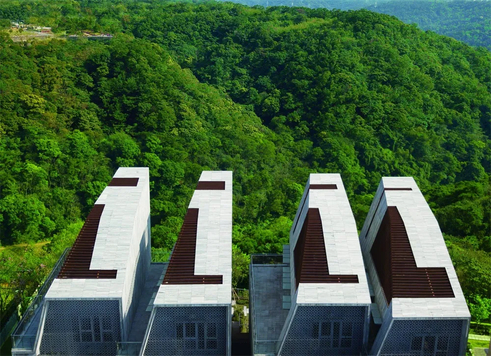 A cluster of four modern cement buildings surrounded by lush greenery on a hillside.