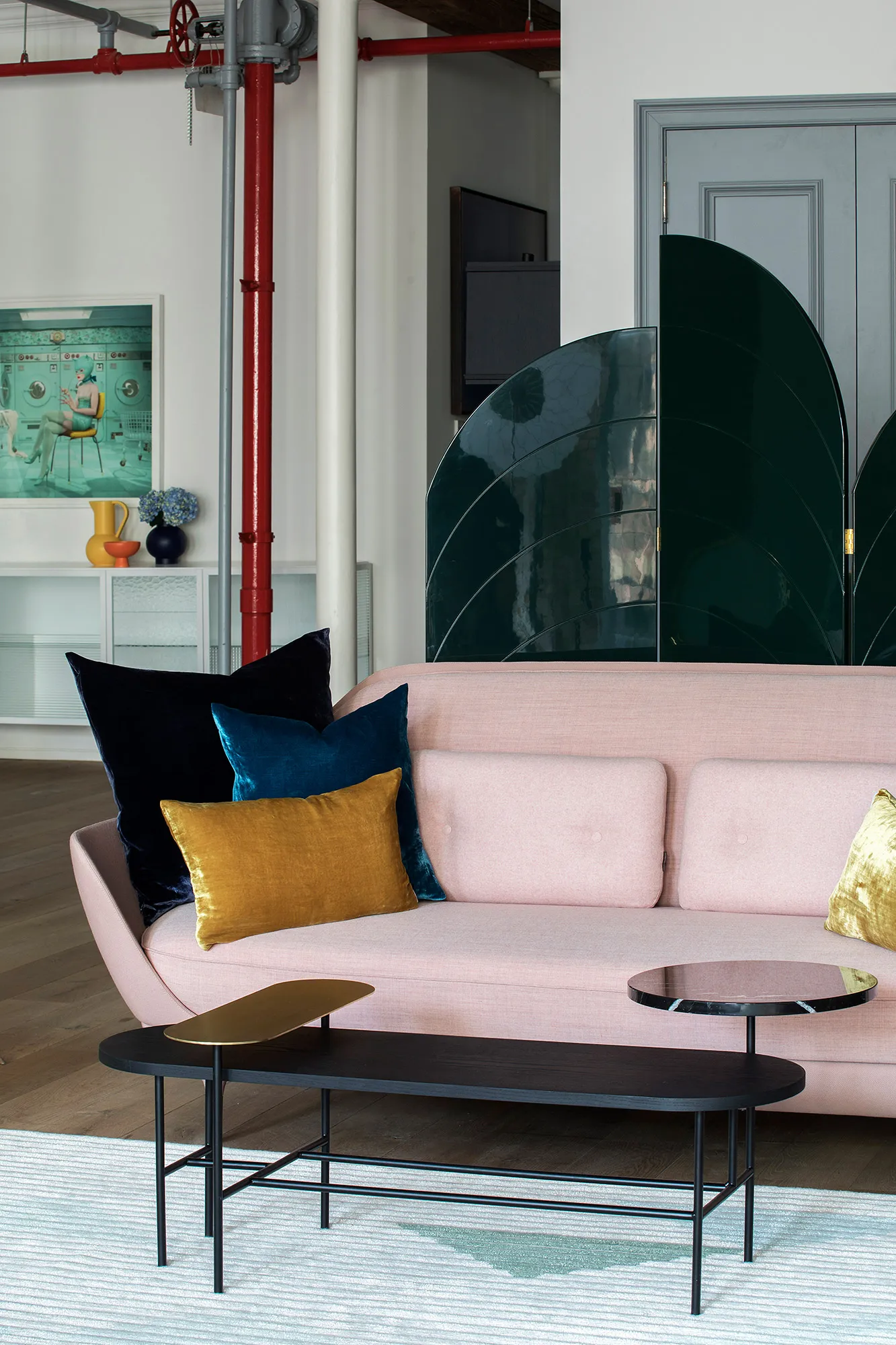 A modern living room featuring a pink couch with assorted cushions, a black metal coffee table with a golden tray, and a uniq