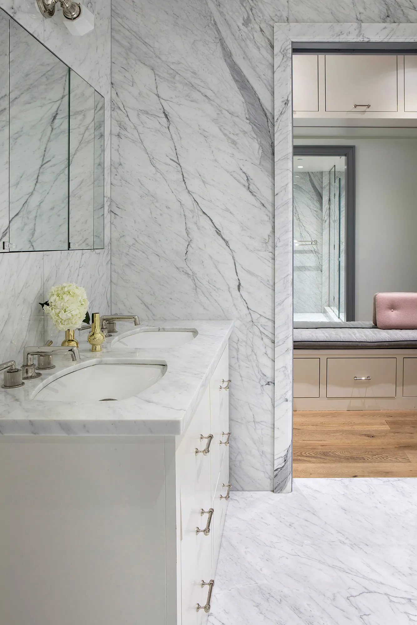 Modern bathroom featuring marble walls and flooring, white cabinets, and a double sink.