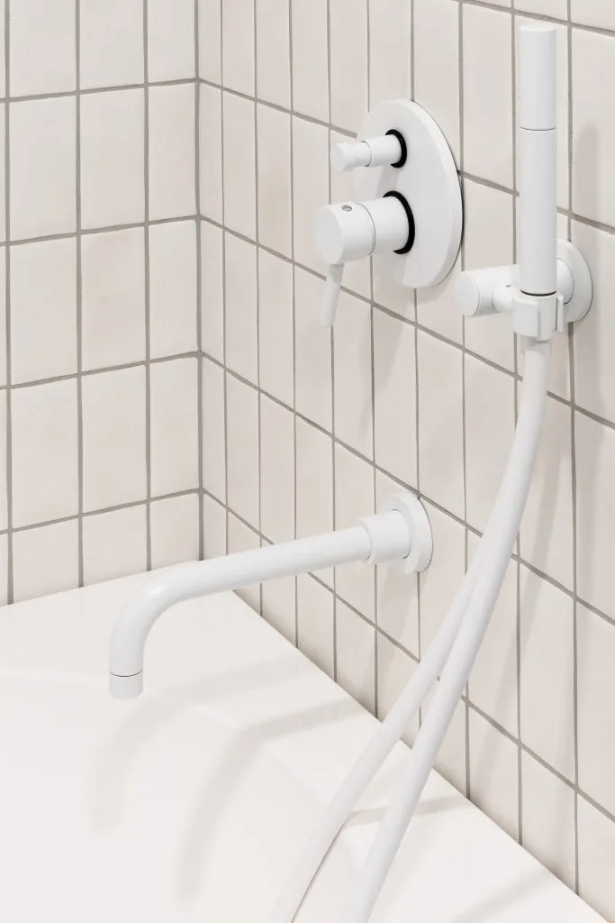 Modern bathroom with white ceramic tiled walls, metal faucet, and white bathtub.