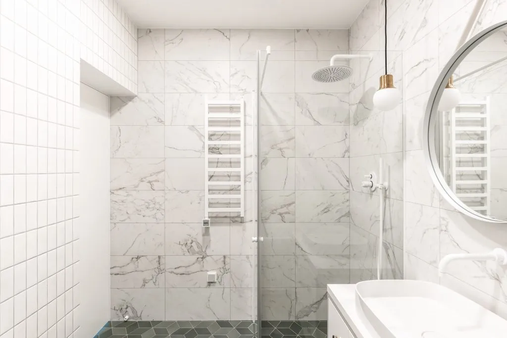 A modern bathroom with marble tiles and a glass shower enclosure.