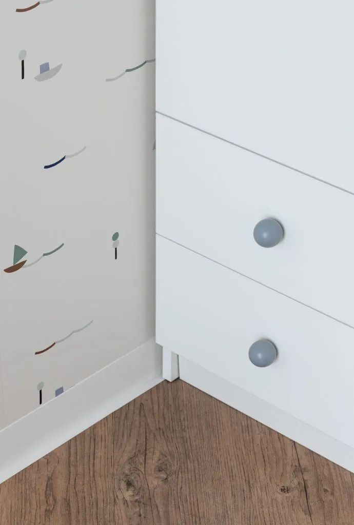 Modern white drawers with blue knobs on wooden floor with printed wallpaper background.