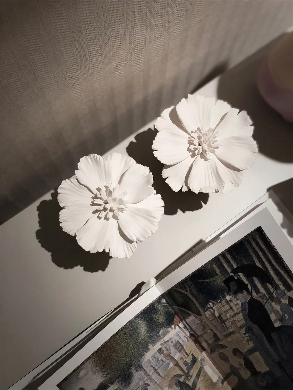 Decorative ceramic floral pieces with long shadows on a shelf.