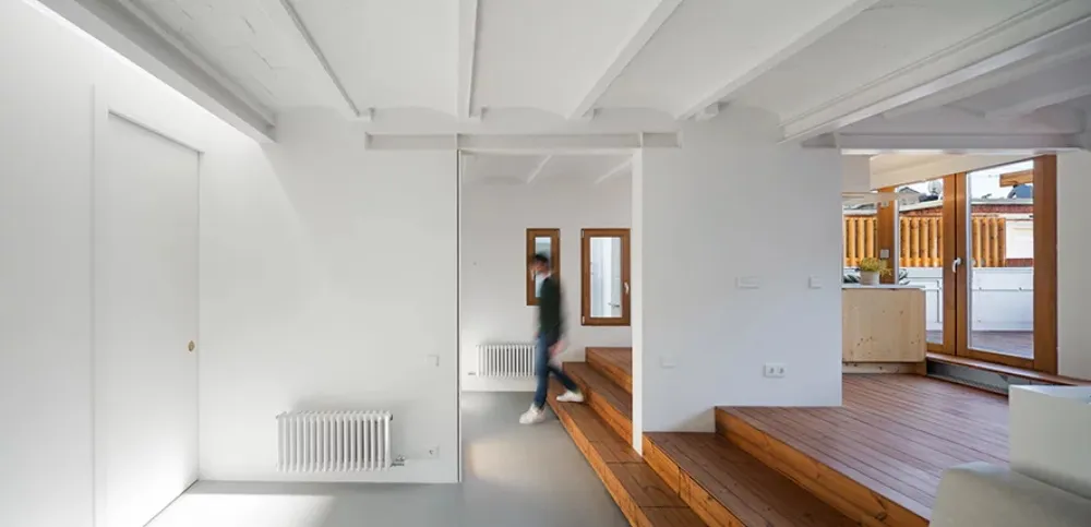 A minimalist apartment with white walls and wooden stairs, showcasing a modern design.