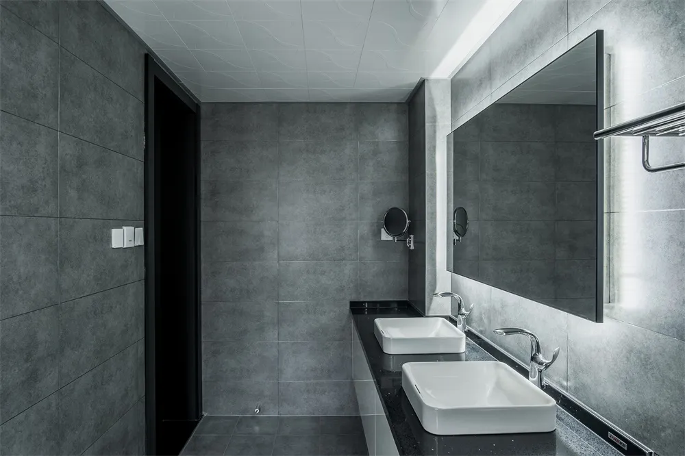 A modern bathroom with black and gray ceramic tiles, a white countertop sink, and a large rectangular mirror.