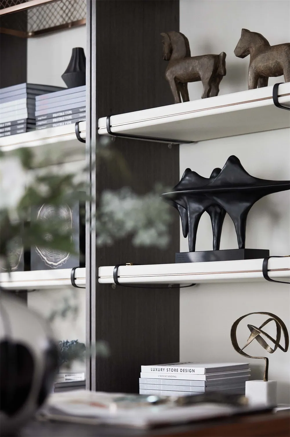 A modern metal shelf with books, horse sculptures, and abstract sculptures.
