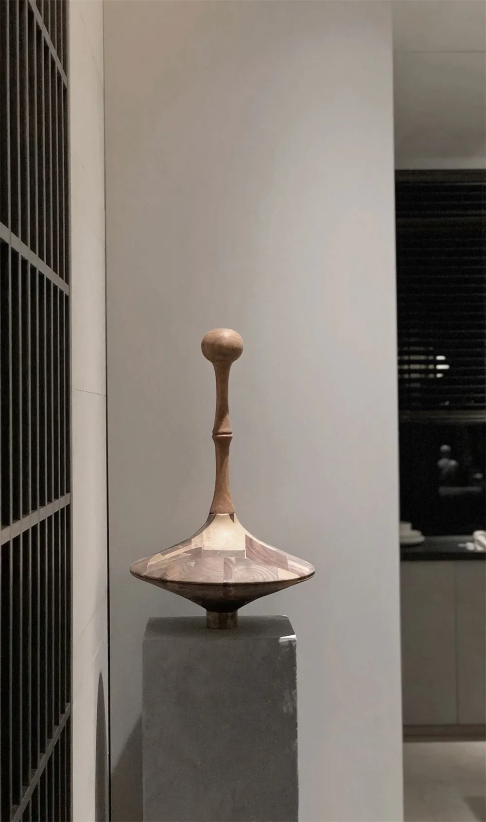 A modern sculpture made of wood with a patchwork design displayed on a pedestal.