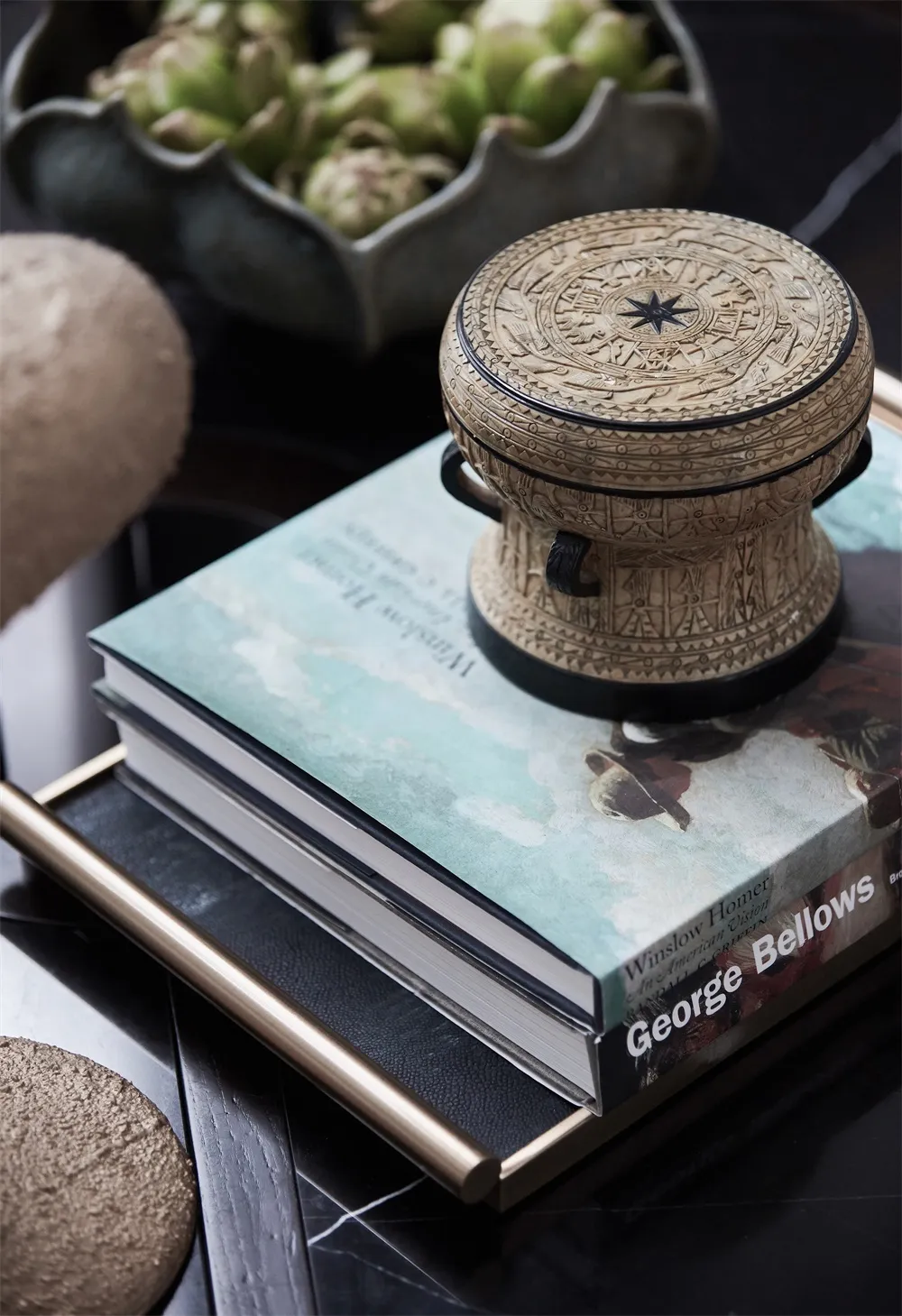 A carved object with intricate designs on a stack of books on a coffee table.