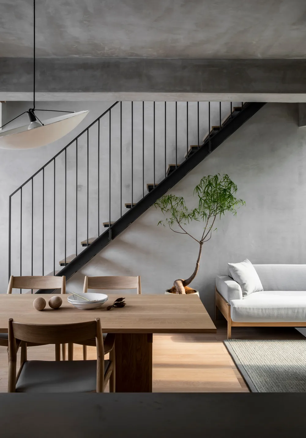 Modern dining room featuring a wooden table, concrete wall, and black metal staircase.