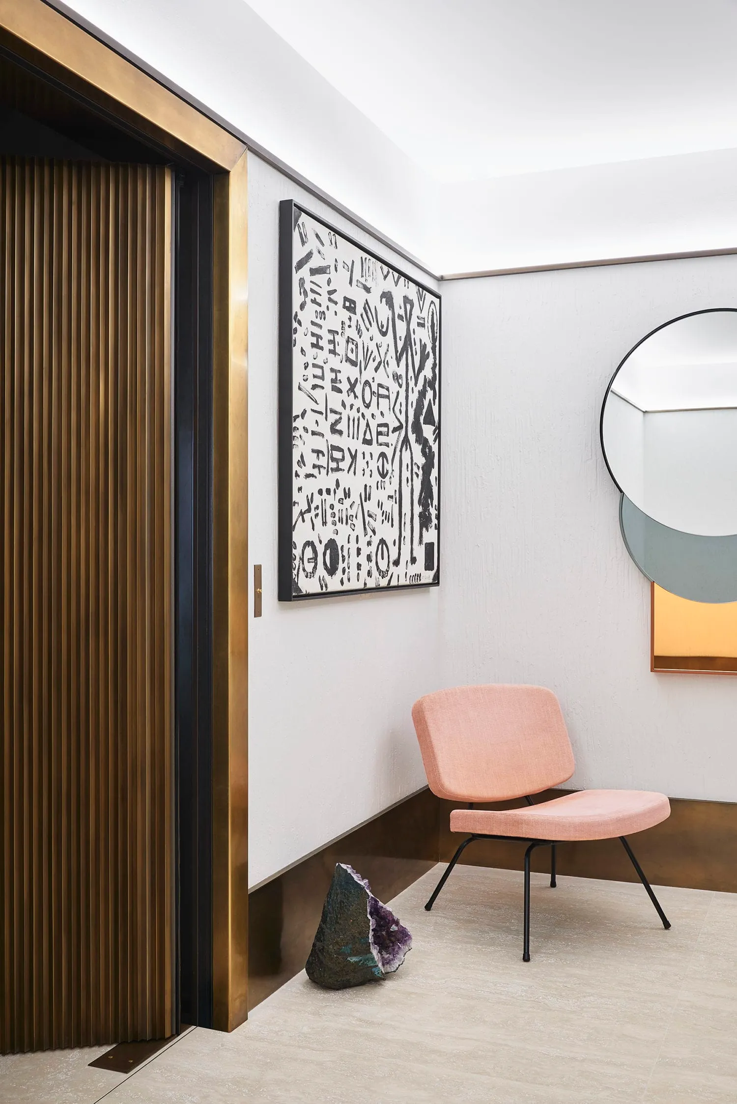 Lobby featuring modern brass and wooden furniture, with a pink upholstered chair and an abstract wall art.