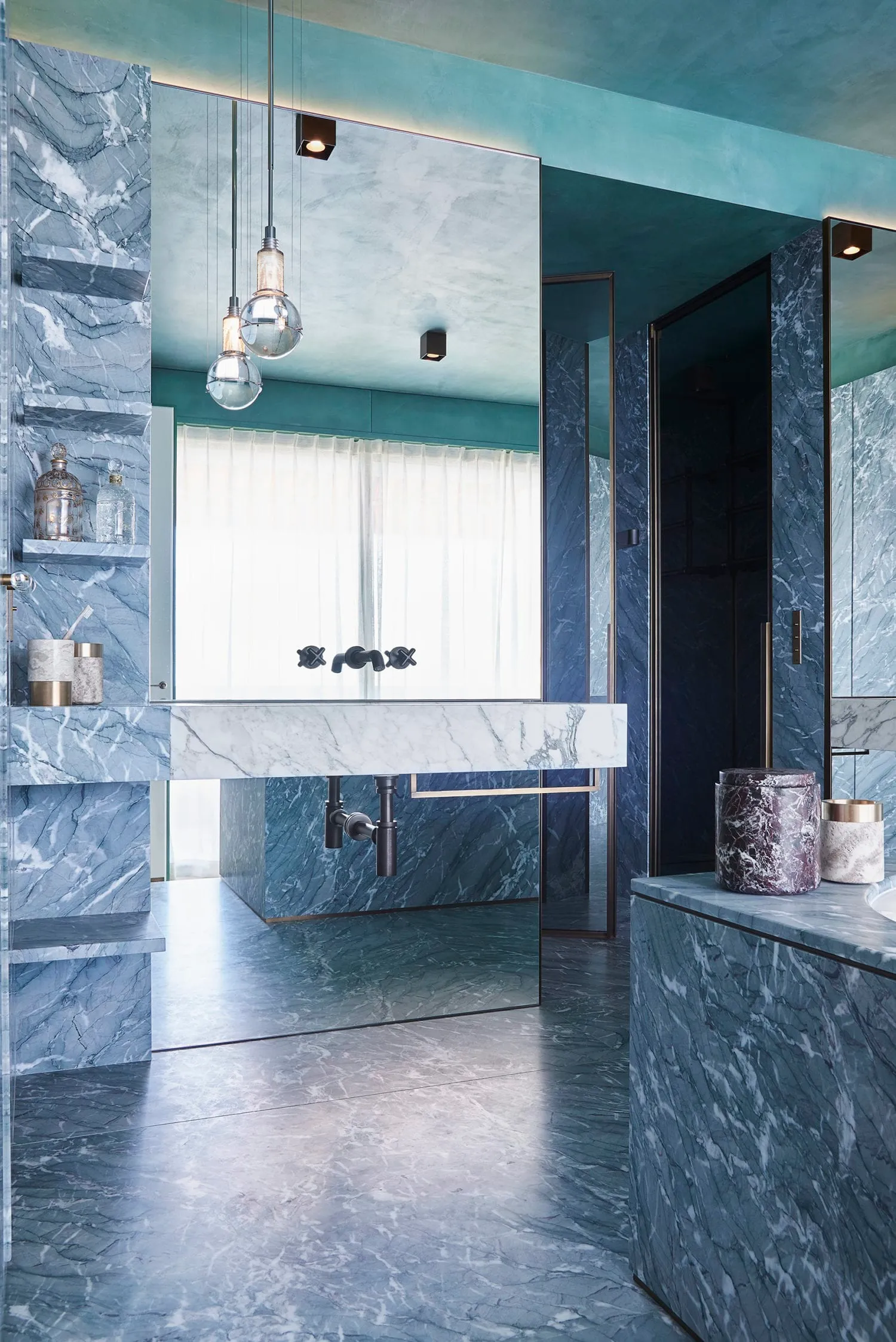 Modern bathroom interior with marble tiles, a floating vanity sink with black faucets, and a large mirror.