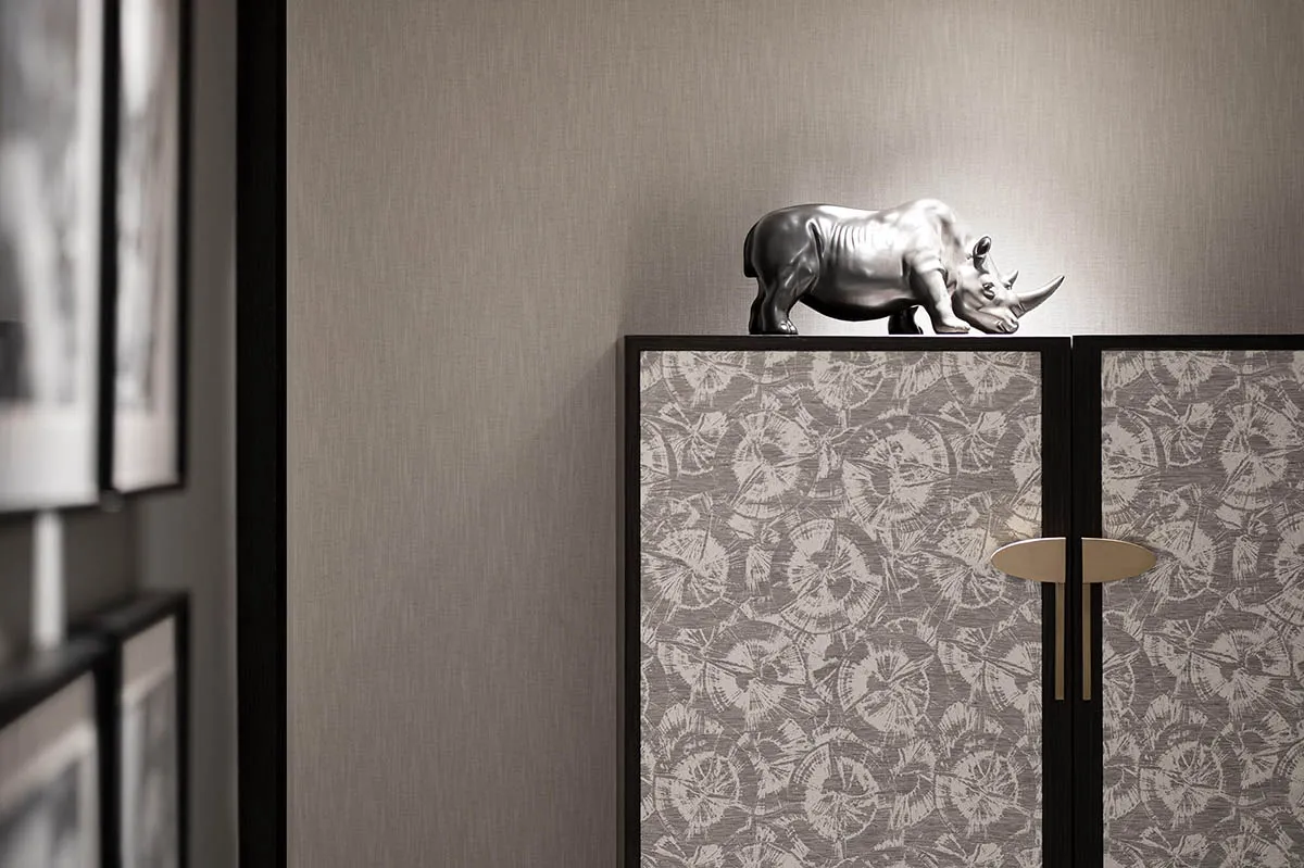 Modern bedroom interior with floral pattern walls and silver rhinoceros statue on cabinet.