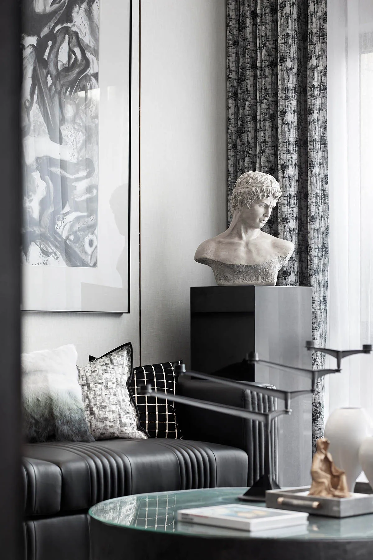 A modern living room featuring a metal and leather sofa with a black and white checkered cushion, a decorative bust, and a gl