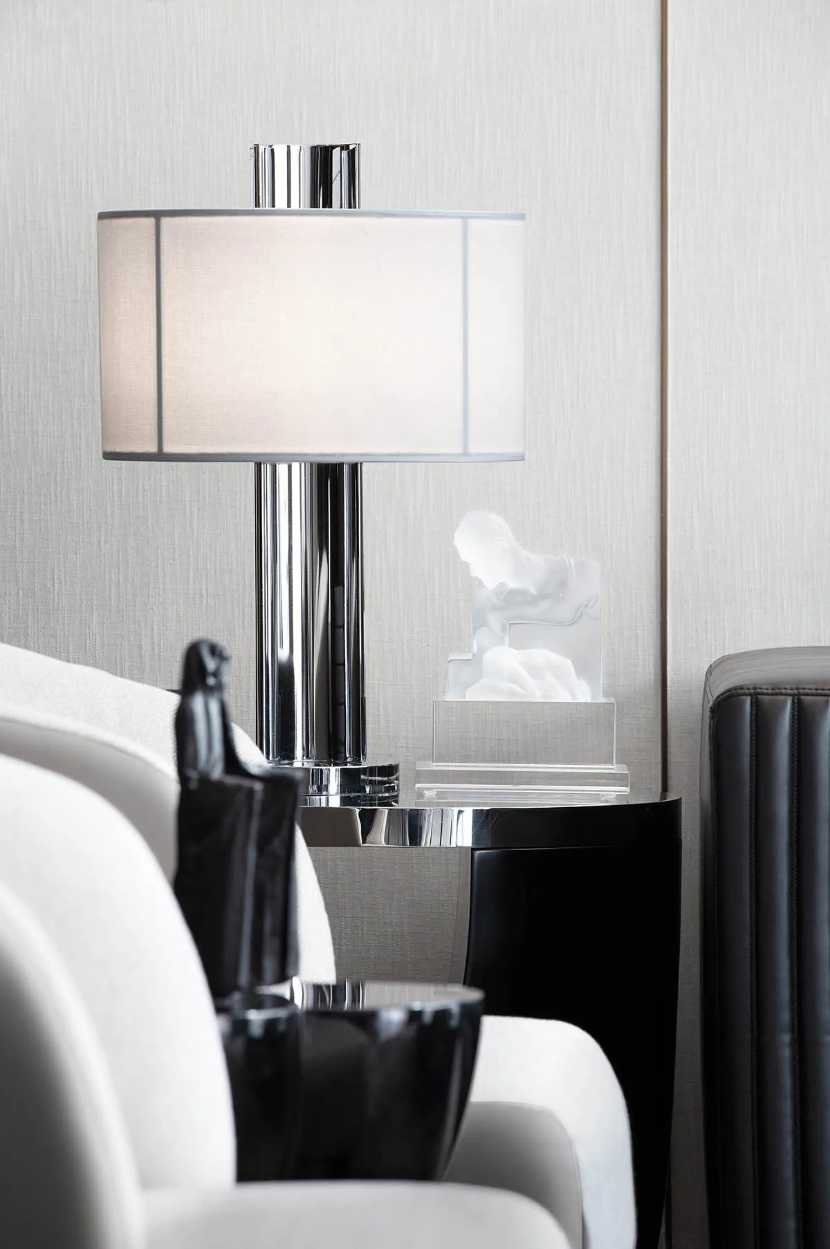 Modern lounge space featuring a glass and chrome table lamp with a white shade, accompanied by a transparent plastic sculptur