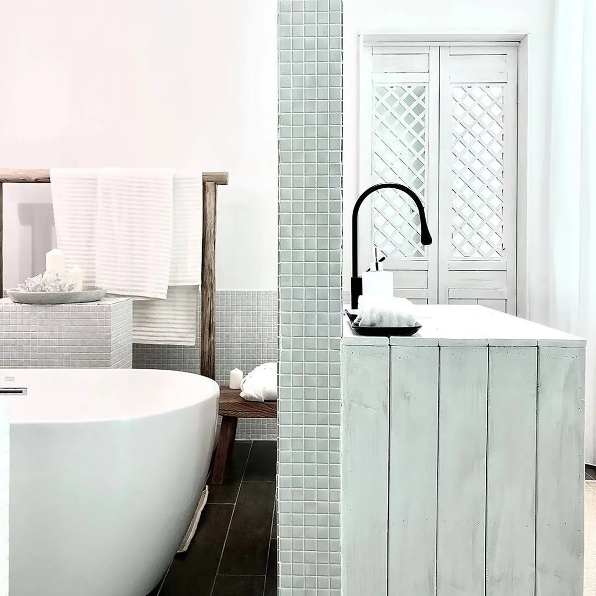 A minimalist bathroom featuring a white bathtub, white tiled walls, and wooden accents.