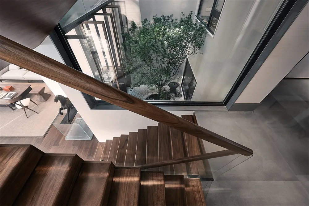 Modern architectural design featuring wooden stairs with glass railing and a central courtyard with a tree and sculpture.