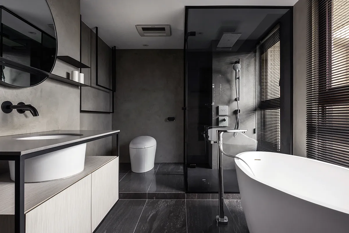 A modern bathroom featuring concrete walls, a freestanding bathtub, and a glass-enclosed shower.